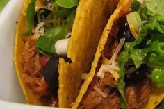 two tacos with meat, lettuce and cheese in a white bowl on a table