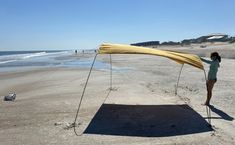 a woman standing on top of a sandy beach next to the ocean holding up a yellow umbrella