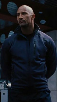 the rock standing in front of a building with his hands on his hips and looking off into the distance