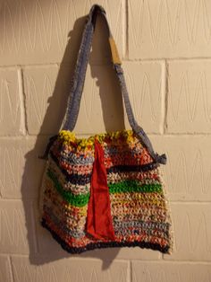 a multicolored purse hanging on a brick wall with a red ribbon attached to it