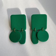 two green square shaped earrings sitting on top of a white cloth covered surface with gold hardware