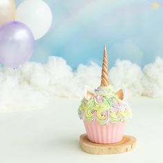 there is a cupcake with a unicorn horn on it and balloons in the background