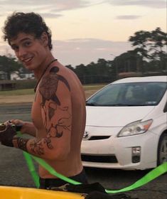 a shirtless man holding a yellow surfboard next to a white car