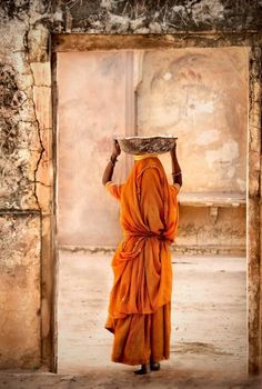 a person in an orange robe carrying a bowl on their head to the door way