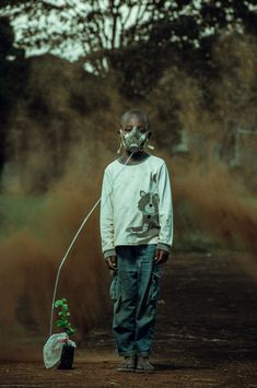 a man wearing a face mask standing in the dirt with a small tree growing out of it