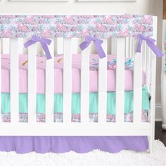 a white crib with pink, blue and green bedding on top of it