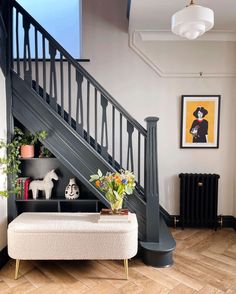 a white bench sitting under a stair case next to a wooden floor and wall with pictures on it