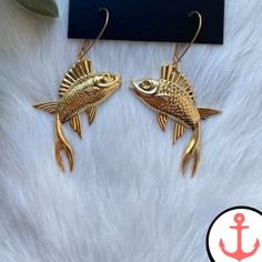 two gold fish shaped earrings sitting on top of a white fur covered floor next to an anchor