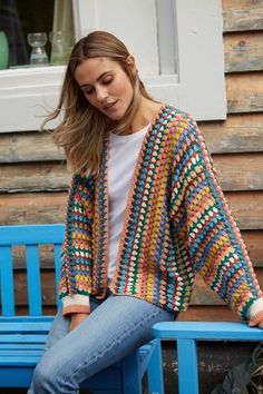 a woman sitting on a blue bench wearing a multicolored crocheted cardigan