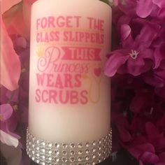 a white candle with pink lettering on it and purple flowers in the back ground behind it