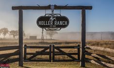 a horse ranch sign hanging from the side of a wooden fence in front of a field