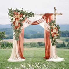 an orange and white wedding arch with flowers on the grass in front of a field