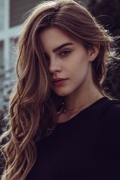 a close up of a person wearing a black shirt with long hair and brown eyes