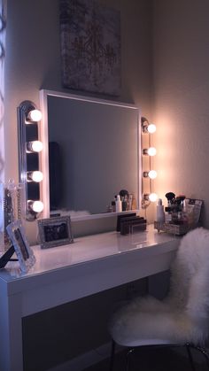 a vanity with lights on and a chair in front of the mirror that is sitting next to it