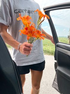 a man is holding flowers out of the car door