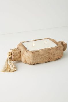 a small wooden candle holder with tassels and a white lit candle in it