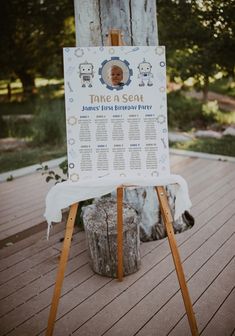 a sign is sitting on a wooden platform in front of a tree trunk with a white table cloth draped over it