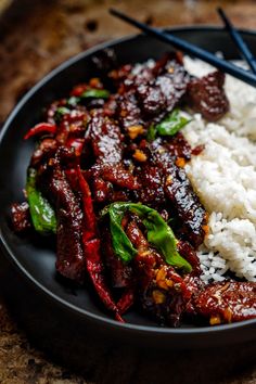 the plate has rice, meat and vegetables with chopsticks in it on the table