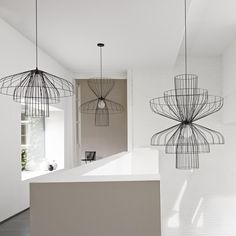 three metal chandeliers hanging from the ceiling above a counter in a white room