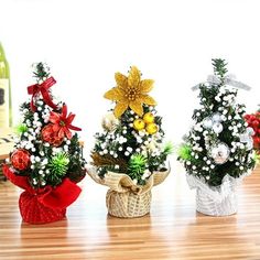 three small christmas trees sitting on top of a wooden table next to a bottle of wine