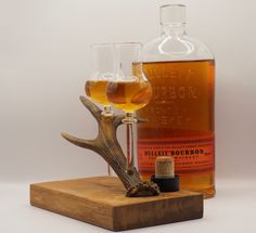 a bottle of bourbon next to two glasses on a wooden block with a deer's antler