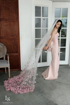 a woman standing in front of a white door wearing a wedding dress and holding a veil over her head