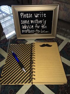 a notepad and pen sitting on top of a notebook next to a sign that says please write some motherly advice for the mother - to be