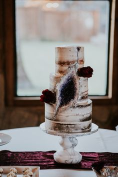 a three tiered cake with flowers on it sitting on a table in front of a window