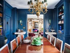 an elegant dining room with blue walls and wooden table surrounded by chairs, chandelier and bookshelves