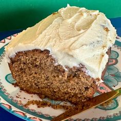 a piece of carrot cake with cream frosting on a plate next to a knife