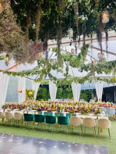 an outdoor event with tables and chairs set up for a formal dinner or function, surrounded by greenery and hanging chandeliers