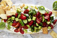 a platter filled with cucumbers, tomatoes and crackers on top of a table