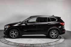 a black bmw suv is parked on a circular concrete platform in a white room with grey walls