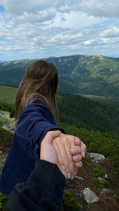 a person holding the hand of another person on top of a hill with mountains in the background