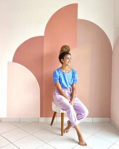 a woman sitting on top of a chair in front of a pink and white wall