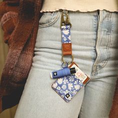 a woman wearing jeans and holding a cell phone strap with a flower pattern on it