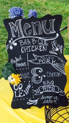 a chalkboard menu sign sitting on top of a yellow cloth covered tablecloth next to a basket filled with flowers