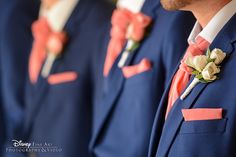 three men in blue suits with pink and white flowers on their lapel covers are lined up