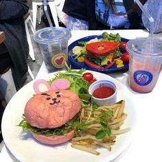 a white plate topped with a sandwich and fries next to plastic cups filled with drinks