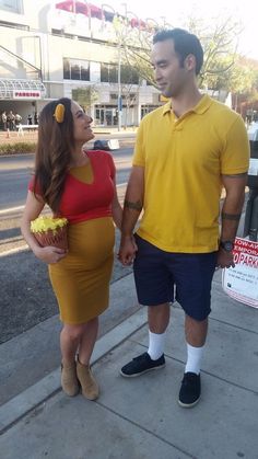 a man and woman dressed in costumes standing next to each other on the sidewalk holding hands