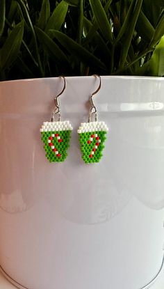 a pair of green and white beaded earrings sitting on top of a potted plant