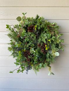 a wreath hanging on the side of a building with pine cones and greenery around it