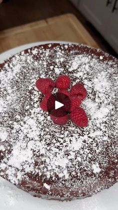 a chocolate cake with powdered sugar and raspberries on top, ready to be eaten