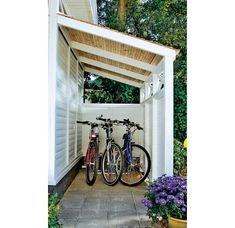 two bikes are parked under a pergolated area on the side of a house