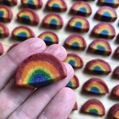 a hand holding a rainbow shaped cookie in front of rows of cookies