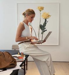 a woman sitting on a chair with a laptop in front of her and a yellow rose behind her