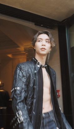 a man with no shirt is standing in front of a glass door wearing a leather jacket