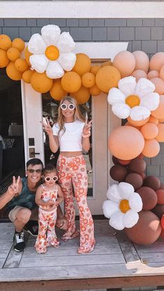 a woman and two children standing in front of a door decorated with orange, white and pink balloons