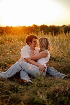 a man and woman sitting on the ground hugging each other in a field at sunset