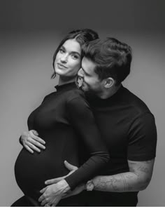 a pregnant woman hugging her husband in black and white